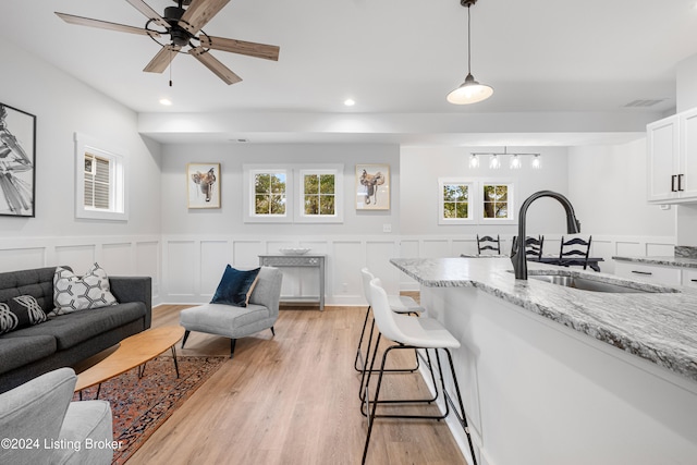 kitchen with sink, light stone countertops, hanging light fixtures, light hardwood / wood-style flooring, and white cabinets