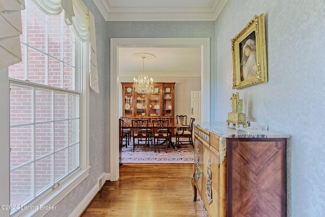 corridor with hardwood / wood-style floors, crown molding, and a notable chandelier