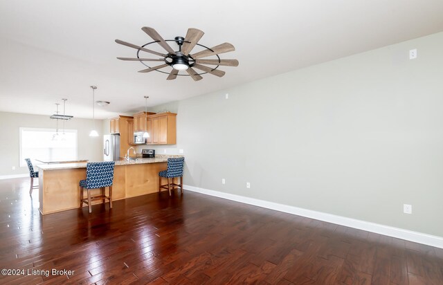 kitchen featuring stainless steel appliances, kitchen peninsula, dark hardwood / wood-style floors, light brown cabinets, and decorative light fixtures