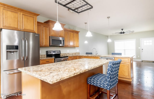 kitchen with a kitchen bar, dark wood-type flooring, kitchen peninsula, ceiling fan, and appliances with stainless steel finishes