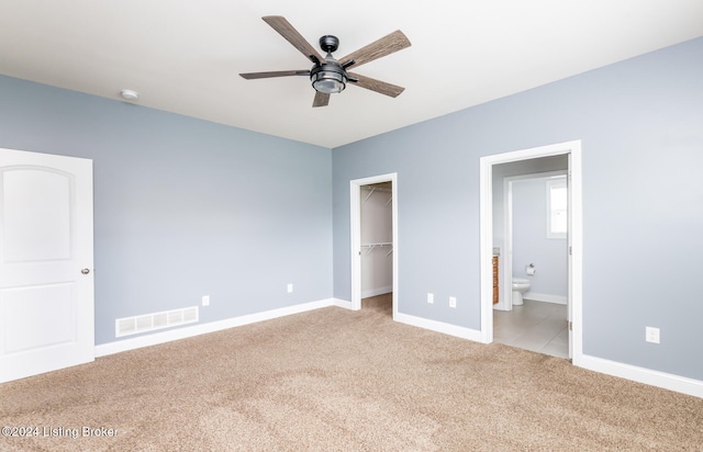 unfurnished bedroom featuring light colored carpet, connected bathroom, ceiling fan, a closet, and a spacious closet