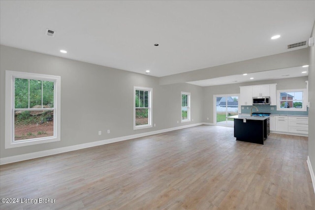 kitchen featuring tasteful backsplash, white cabinetry, an island with sink, and light hardwood / wood-style floors