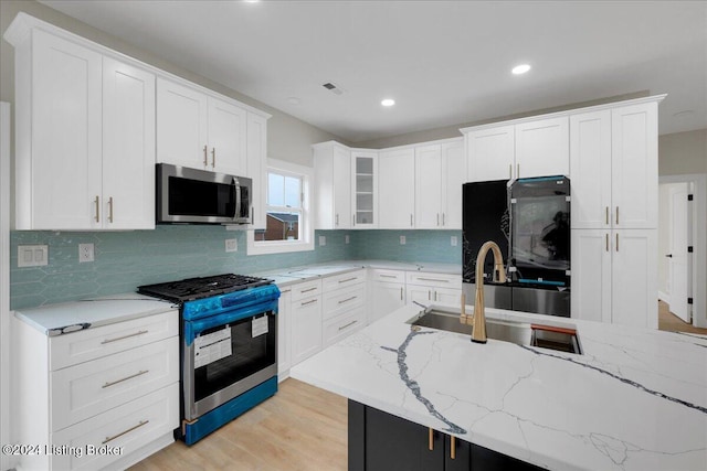 kitchen featuring sink, light stone countertops, white cabinetry, light wood-type flooring, and appliances with stainless steel finishes