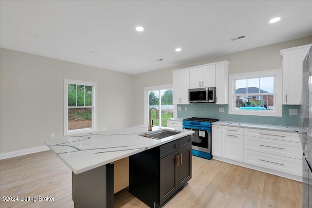 kitchen with a center island with sink, white cabinetry, appliances with stainless steel finishes, sink, and light hardwood / wood-style flooring