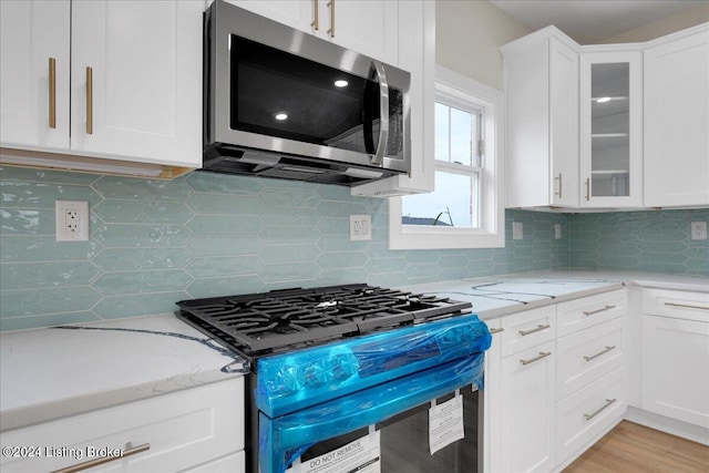 kitchen featuring white cabinets, light stone countertops, black gas range oven, and tasteful backsplash