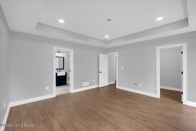 unfurnished bedroom featuring ensuite bathroom, hardwood / wood-style floors, a spacious closet, and a raised ceiling