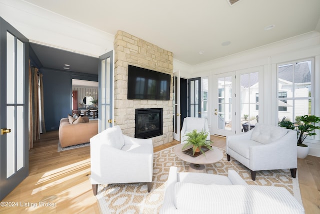 living room featuring a stone fireplace, ornamental molding, and light hardwood / wood-style flooring