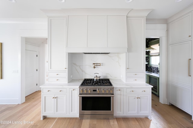 kitchen with white cabinetry, stainless steel range, light wood-type flooring, and backsplash