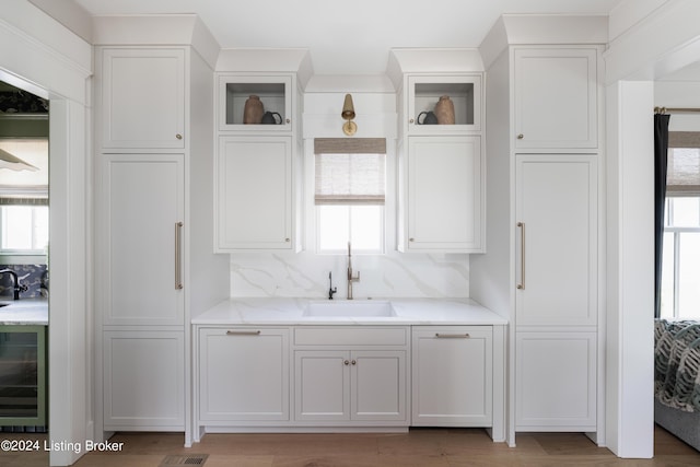 bar with backsplash, sink, light hardwood / wood-style floors, white cabinets, and beverage cooler