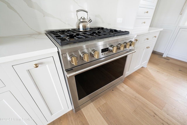 kitchen featuring white cabinets, light stone countertops, high end range, and light hardwood / wood-style flooring