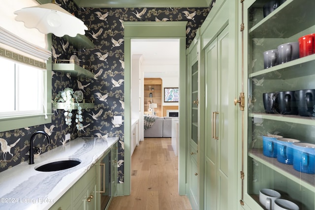 bar with green cabinets, sink, light hardwood / wood-style flooring, and light stone counters