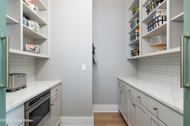 interior space featuring stainless steel microwave, light stone counters, light wood-type flooring, and backsplash