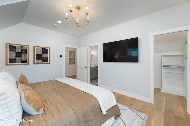 bedroom featuring connected bathroom, an inviting chandelier, vaulted ceiling, and light hardwood / wood-style flooring