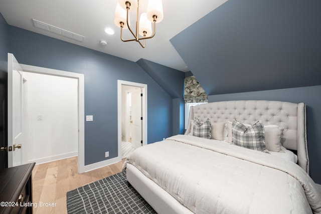 bedroom featuring connected bathroom, lofted ceiling, an inviting chandelier, and light hardwood / wood-style flooring