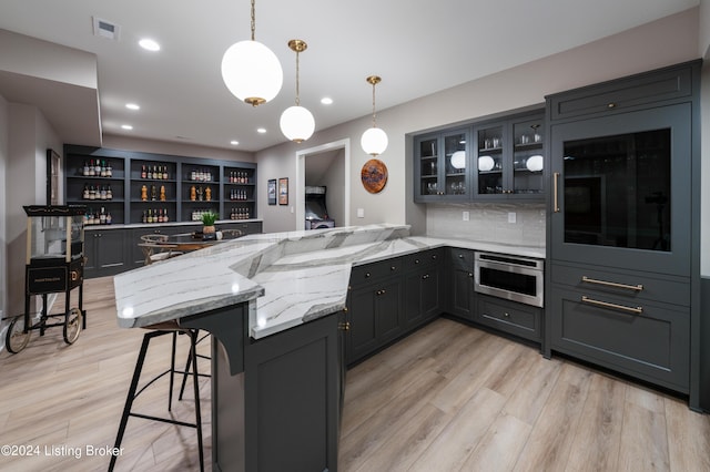 kitchen featuring light hardwood / wood-style floors, kitchen peninsula, a kitchen bar, decorative light fixtures, and oven