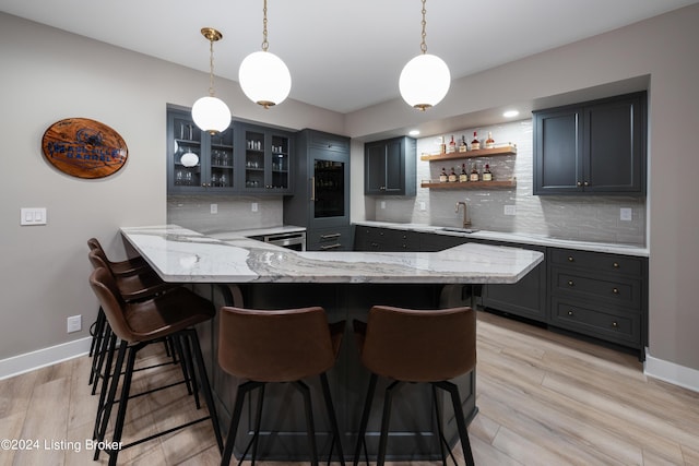 kitchen featuring kitchen peninsula, a kitchen breakfast bar, backsplash, hanging light fixtures, and light hardwood / wood-style flooring