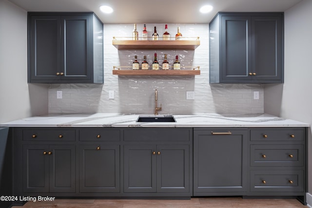 bar featuring tasteful backsplash, sink, light stone counters, and gray cabinetry