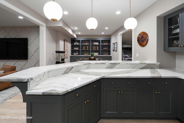 kitchen with light stone counters, kitchen peninsula, backsplash, light hardwood / wood-style flooring, and pendant lighting