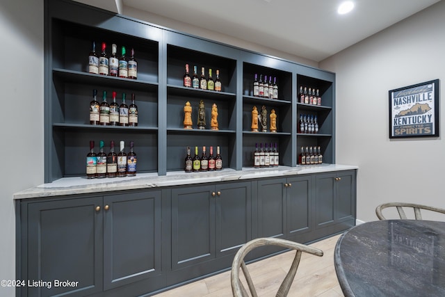 bar with light stone countertops, gray cabinetry, and light wood-type flooring