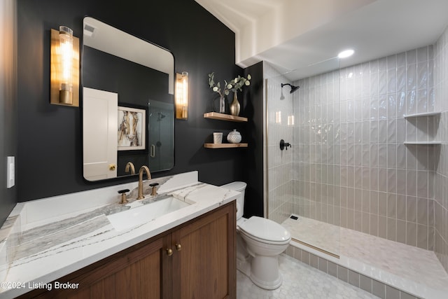 bathroom with toilet, vanity, tile patterned flooring, and tiled shower