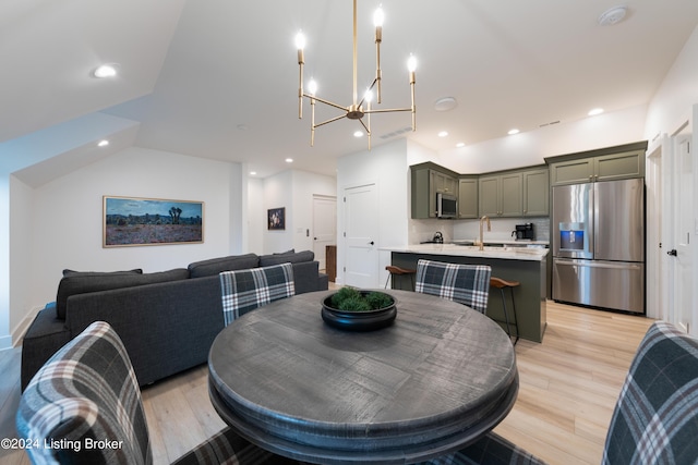 dining area with sink, a chandelier, vaulted ceiling, and light hardwood / wood-style flooring