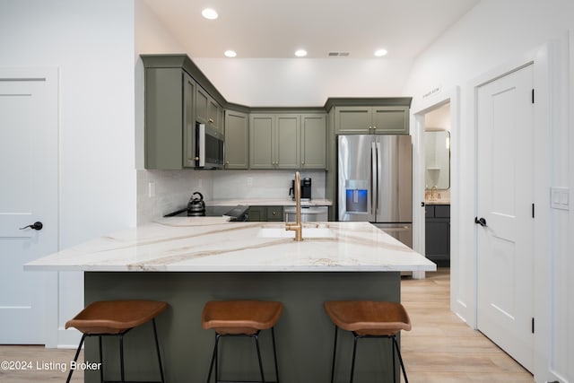 kitchen featuring appliances with stainless steel finishes, light stone countertops, decorative backsplash, light hardwood / wood-style floors, and a breakfast bar