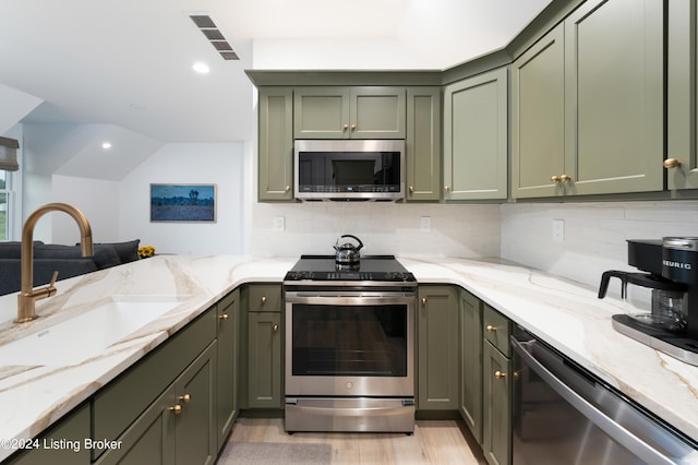 kitchen with green cabinets, sink, appliances with stainless steel finishes, backsplash, and light hardwood / wood-style flooring