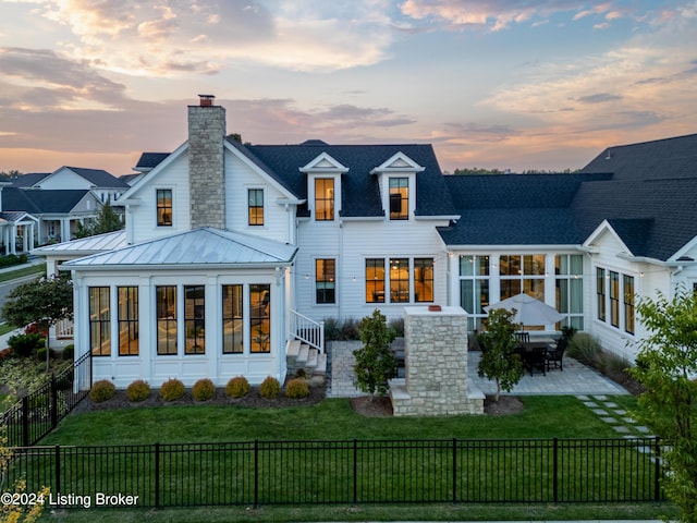 back house at dusk featuring a patio, a sunroom, and a yard