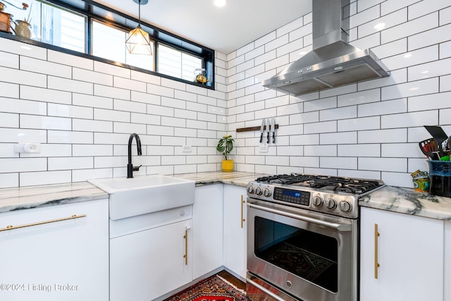 kitchen with decorative light fixtures, decorative backsplash, stainless steel range, white cabinets, and wall chimney exhaust hood