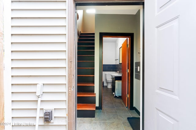 corridor featuring dark tile patterned flooring, tile walls, and sink