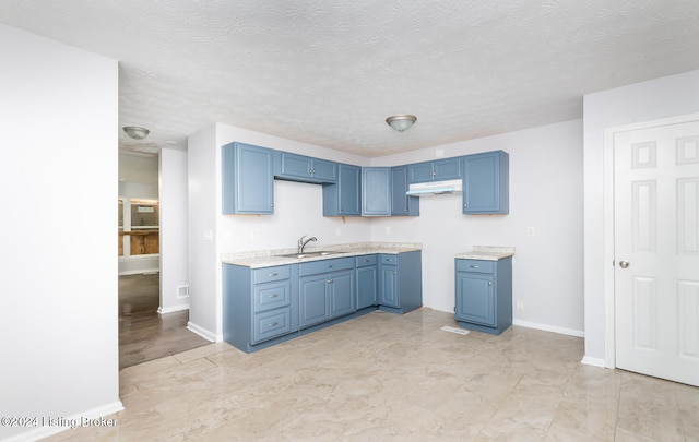 kitchen with blue cabinetry, a textured ceiling, and sink