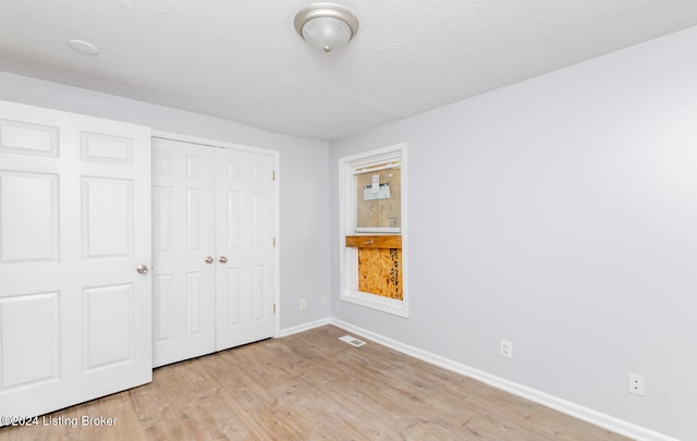 unfurnished bedroom featuring light hardwood / wood-style floors, a textured ceiling, and a closet