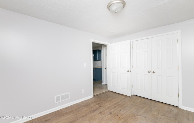 unfurnished bedroom featuring light hardwood / wood-style floors, a textured ceiling, and a closet