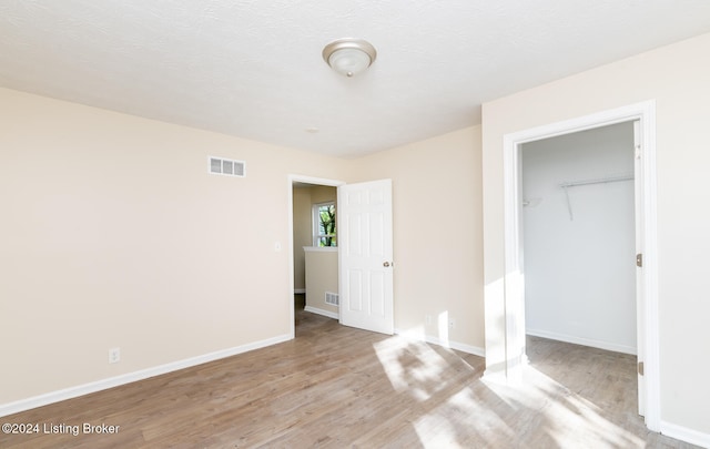 unfurnished bedroom featuring a textured ceiling, a closet, light hardwood / wood-style flooring, and a spacious closet