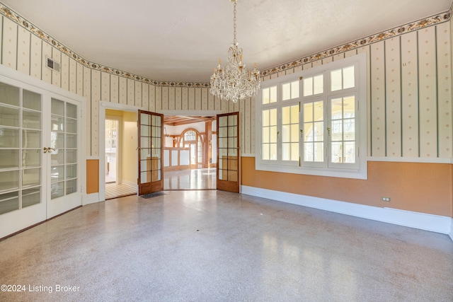 empty room featuring french doors, a textured ceiling, and an inviting chandelier