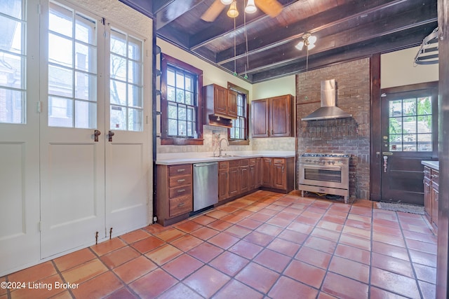 kitchen featuring beam ceiling, a wealth of natural light, wall chimney range hood, and appliances with stainless steel finishes