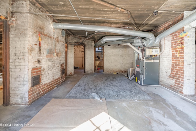 basement featuring heating unit and brick wall