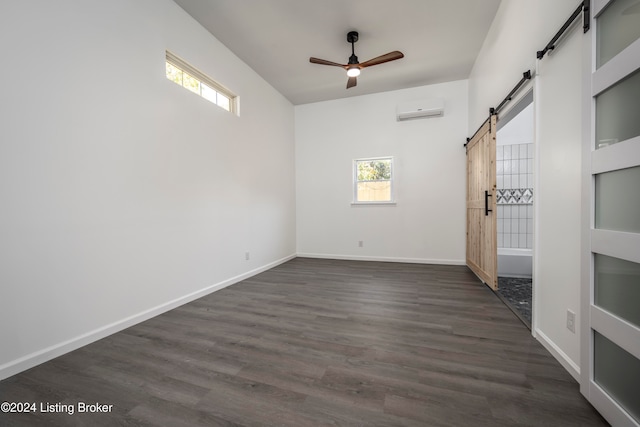 empty room with a wall mounted AC, dark hardwood / wood-style flooring, a barn door, and ceiling fan