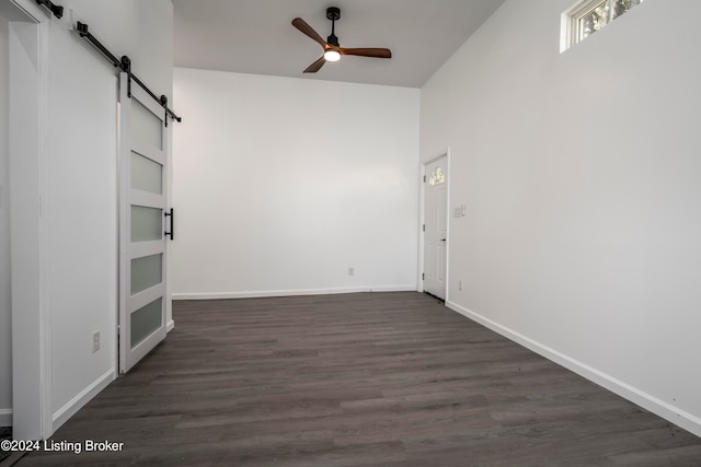 unfurnished room with a barn door, dark hardwood / wood-style floors, and ceiling fan