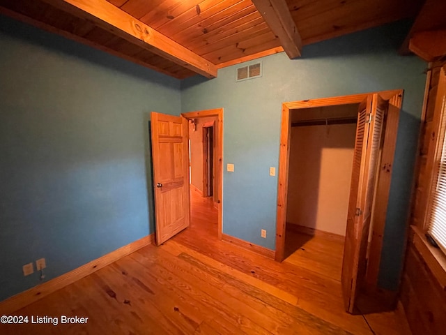 unfurnished bedroom featuring light hardwood / wood-style floors, beamed ceiling, wood ceiling, and a closet