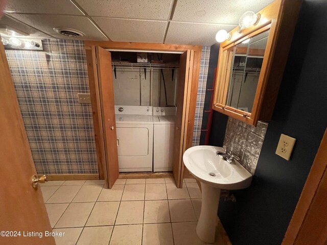 bathroom featuring tile patterned flooring, decorative backsplash, a paneled ceiling, sink, and washer and clothes dryer