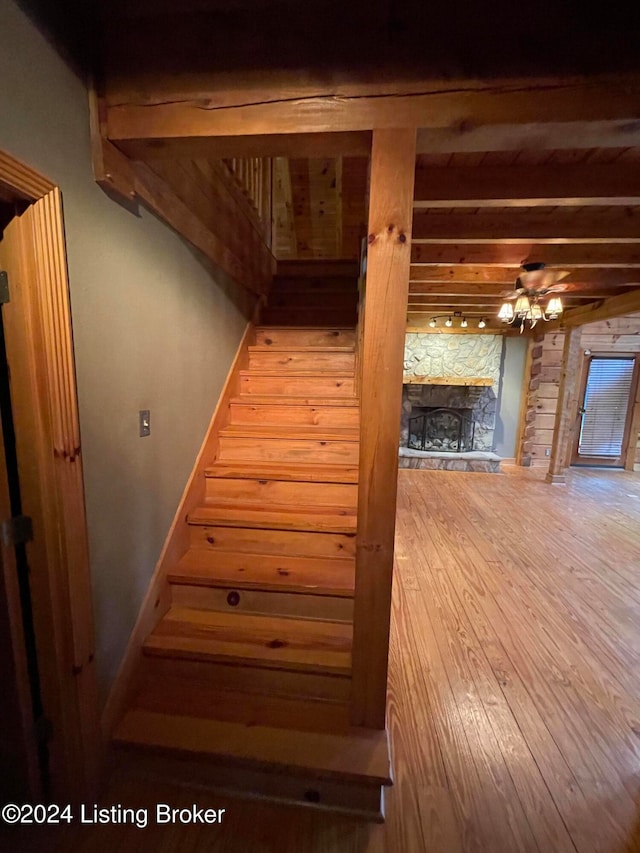 staircase featuring hardwood / wood-style floors, a fireplace, beamed ceiling, and ceiling fan