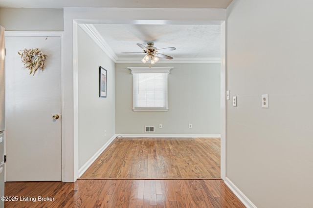 empty room featuring visible vents, crown molding, baseboards, and wood finished floors