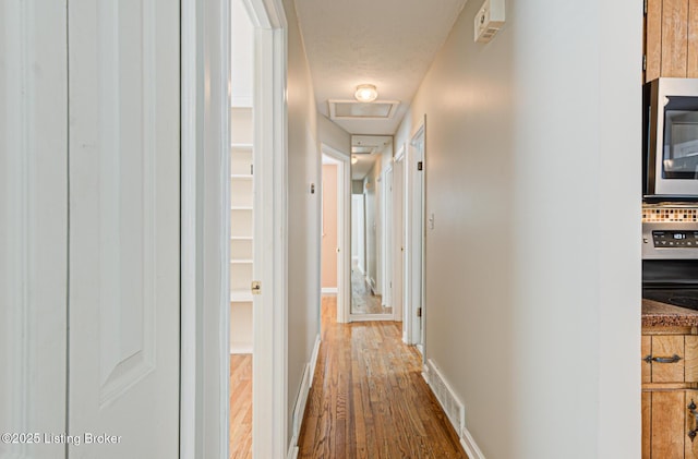 hallway with attic access, visible vents, baseboards, and wood finished floors