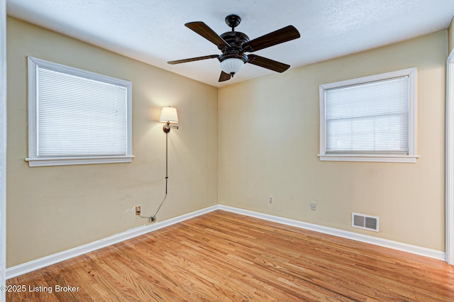 empty room with a textured ceiling, light wood finished floors, visible vents, and baseboards