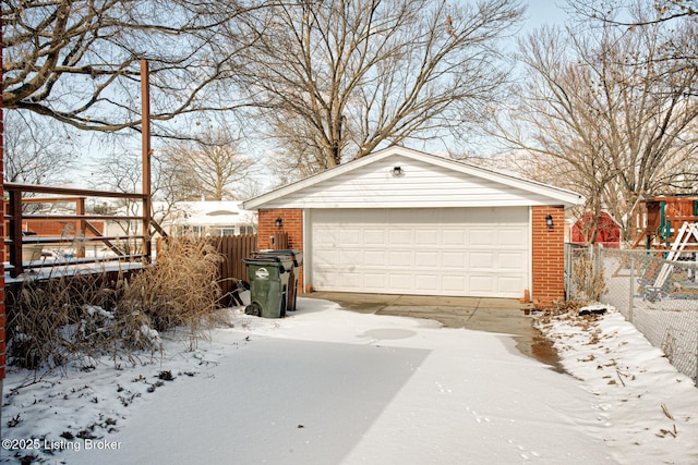 snow covered garage with a detached garage and fence