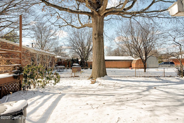 yard layered in snow featuring an outbuilding, a shed, and fence