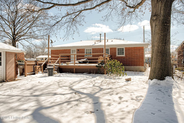 snow covered house with brick siding and a wooden deck