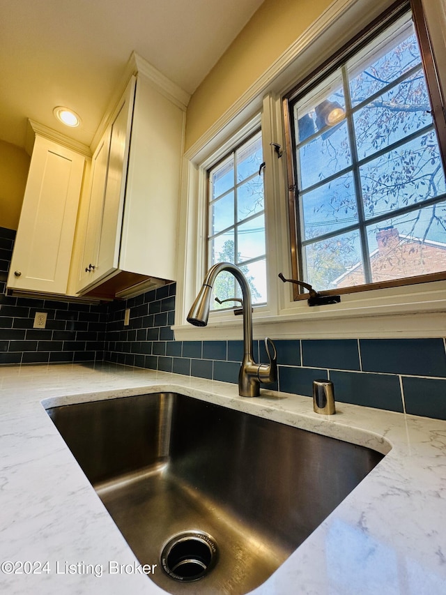 room details with light stone counters, white cabinetry, sink, and tasteful backsplash