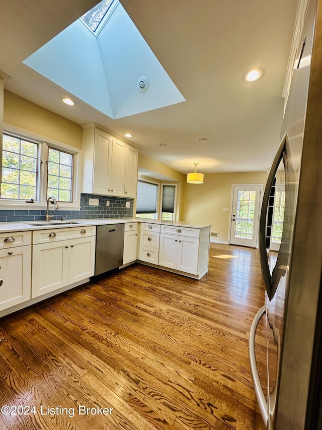 kitchen featuring kitchen peninsula, appliances with stainless steel finishes, a skylight, sink, and pendant lighting